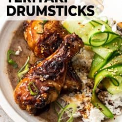 Two chicken drumsticks on a white plate with rice an cucumber ribbons.