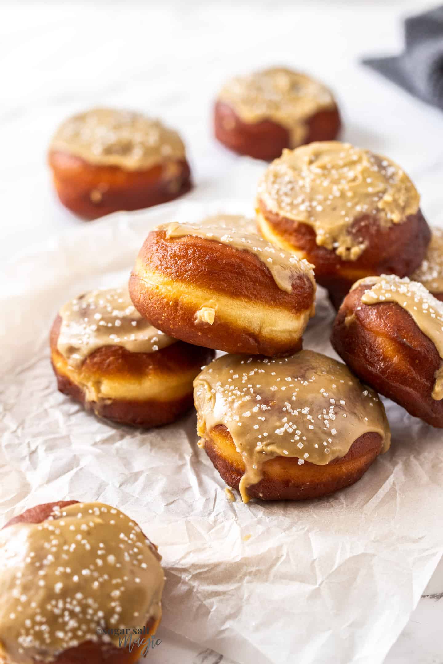 A pile of doughnuts topped with caramel icing on a sheet of baking paper.