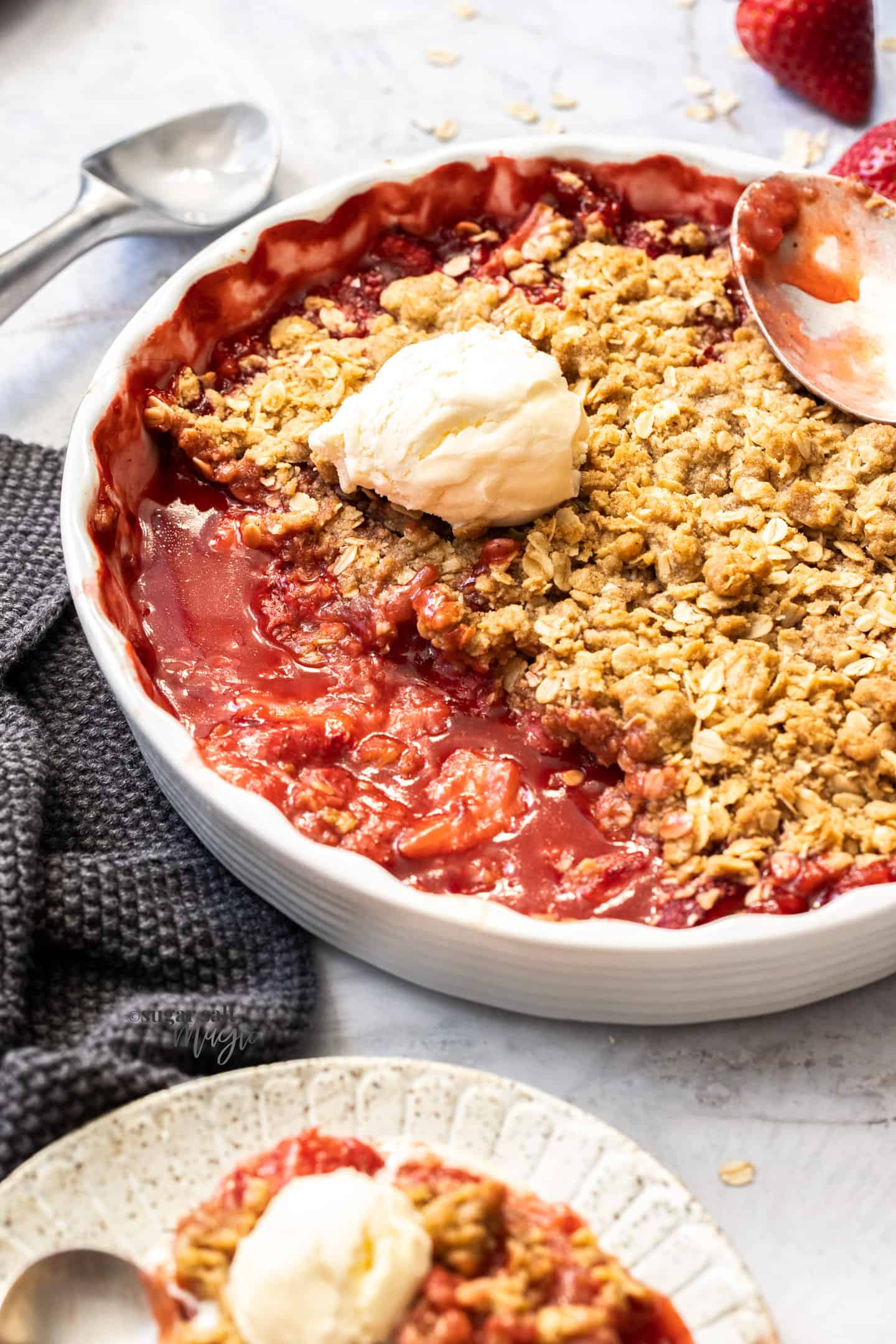 A white pie dish filled with baked strawberry crisp with a dollop of ice cream on top.