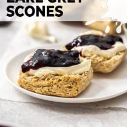 A scone broken in half and topped with cream and jam.