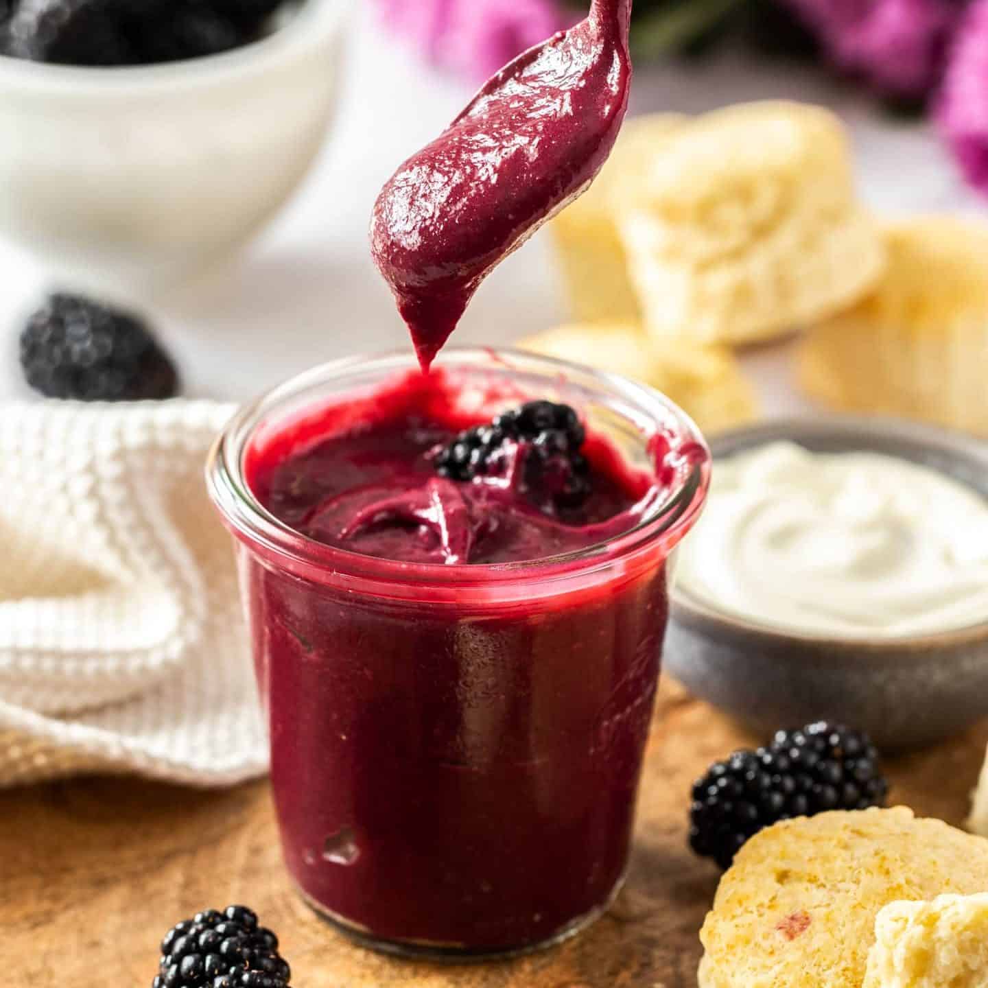A spoon hovering above a jar of blackberry curd