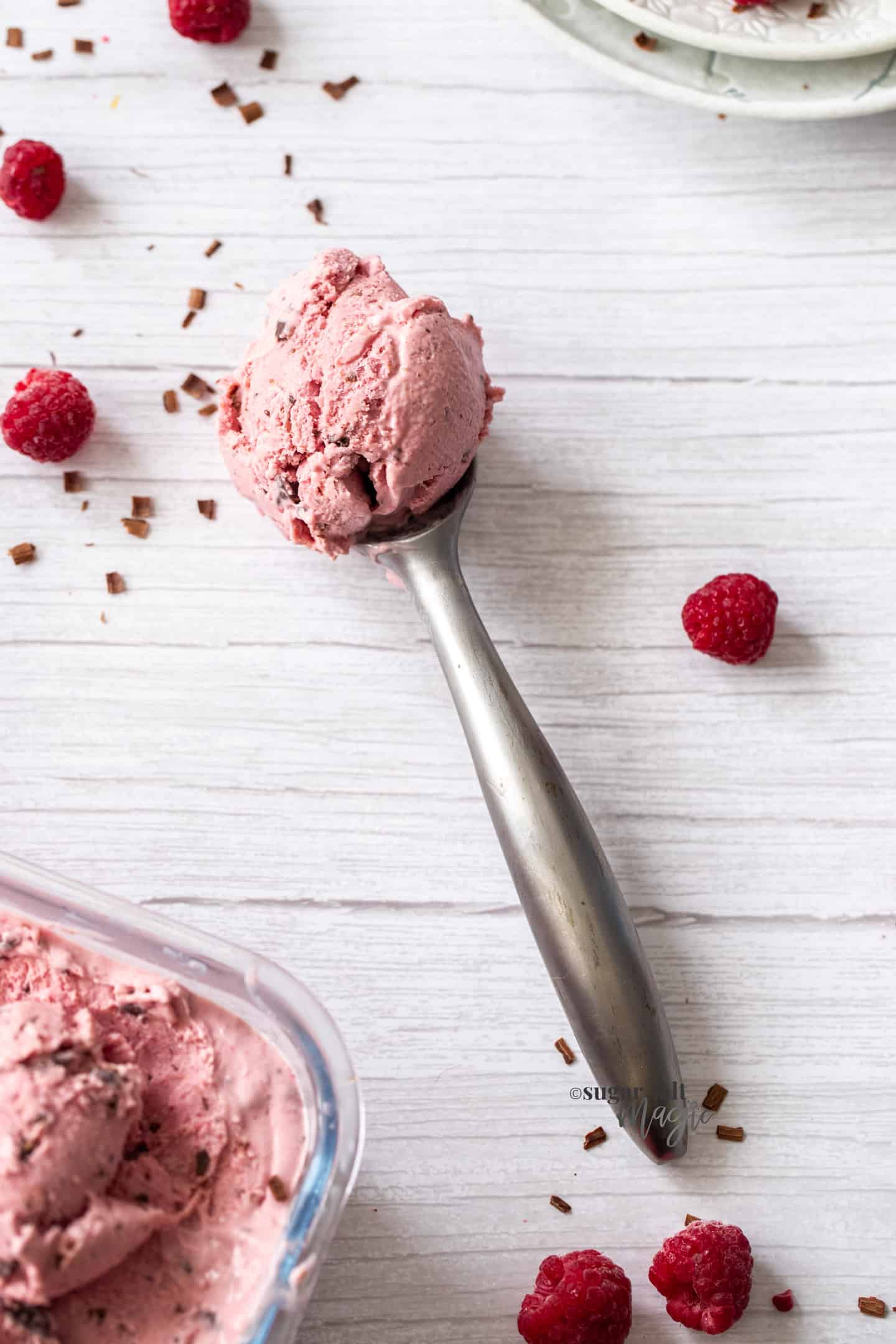 A silver ice cream scoop filled with scoop of raspberry ice cream.