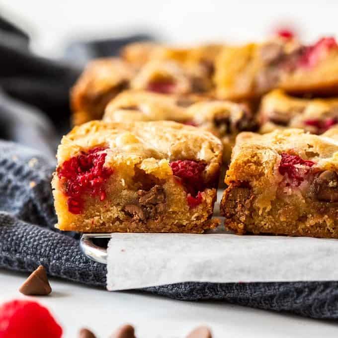 Close up of the side of some blondies with raspberries and chocolate chips nearby.