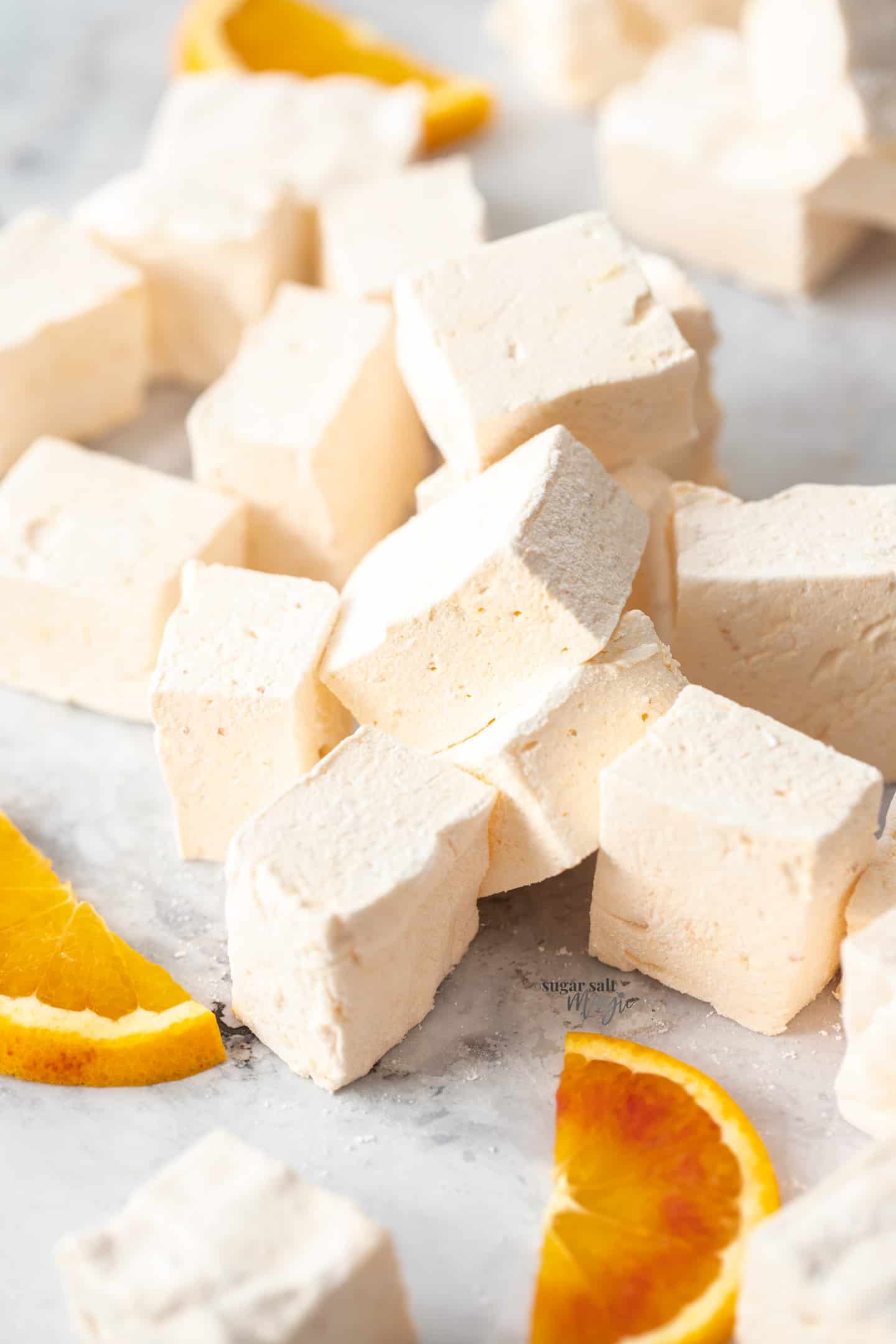 A pile of orange marshmallows on a grey marble surface.
