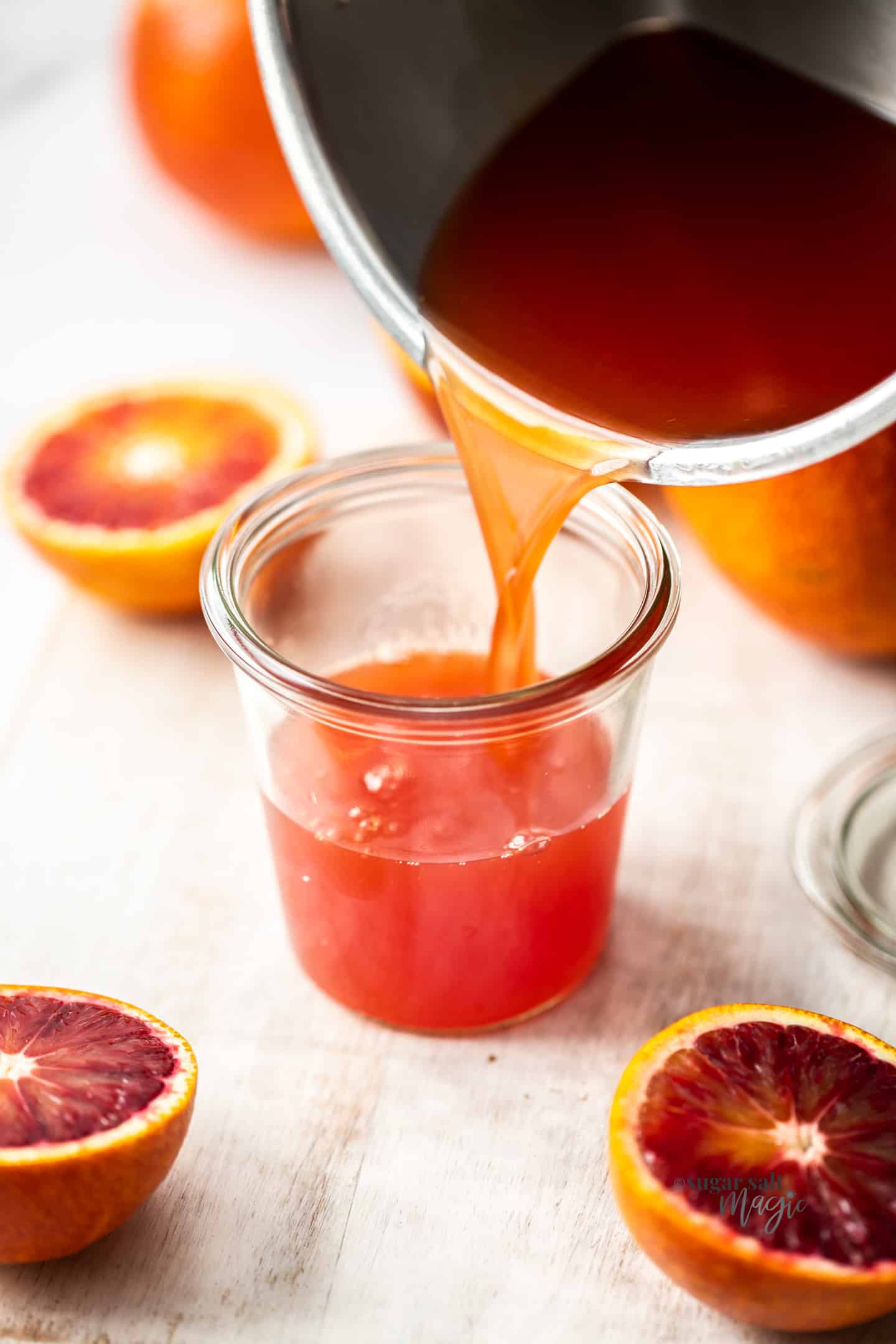 Orange simple syrup being poured into a glass jar.