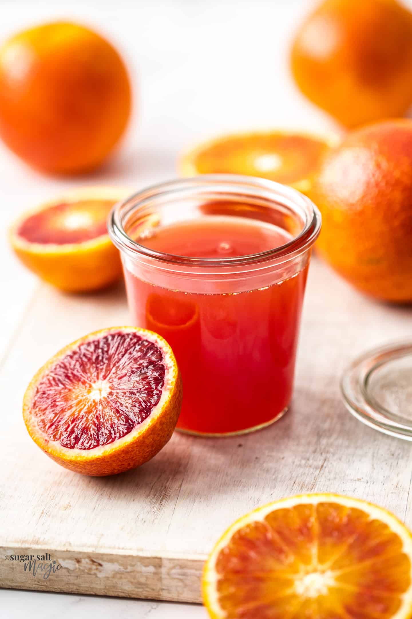 A preserving jar, filled with blood orange syrup surrounded by oranges.