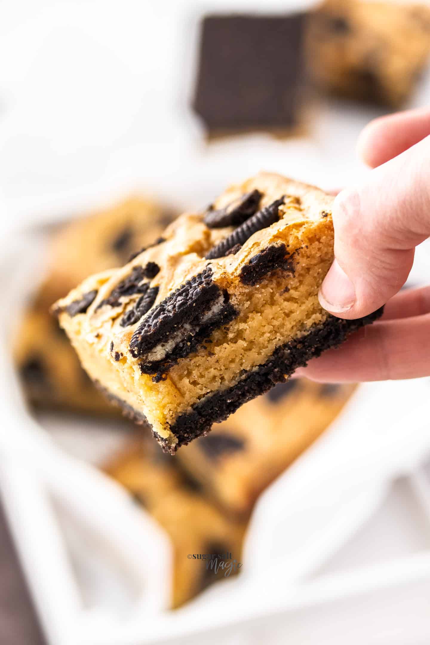 A hand holding an Oreo blondie, showing the inside texture.