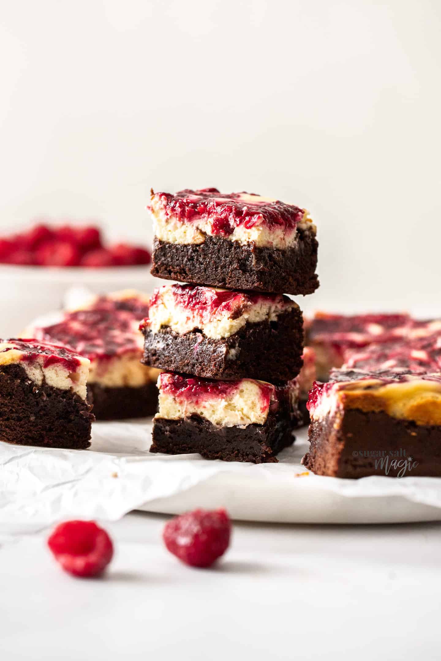 A stack of 3 raspberry topped brownies on a marble cake plate.