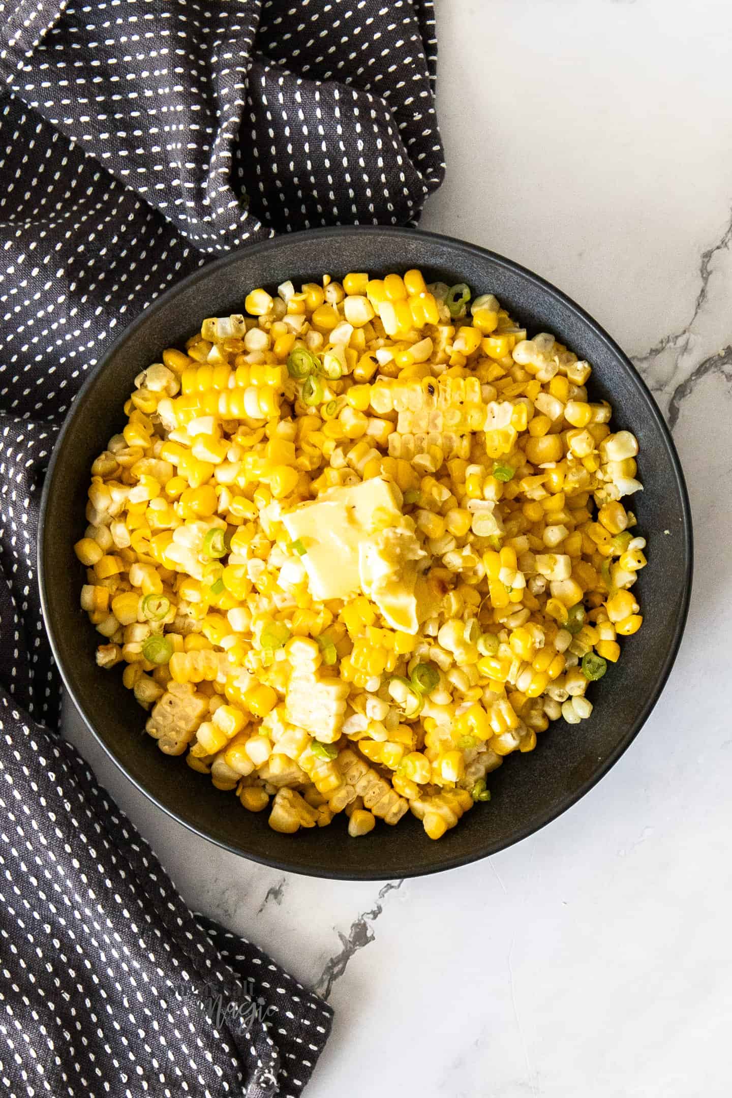 A black bowl, filled with cooked corn kernels.