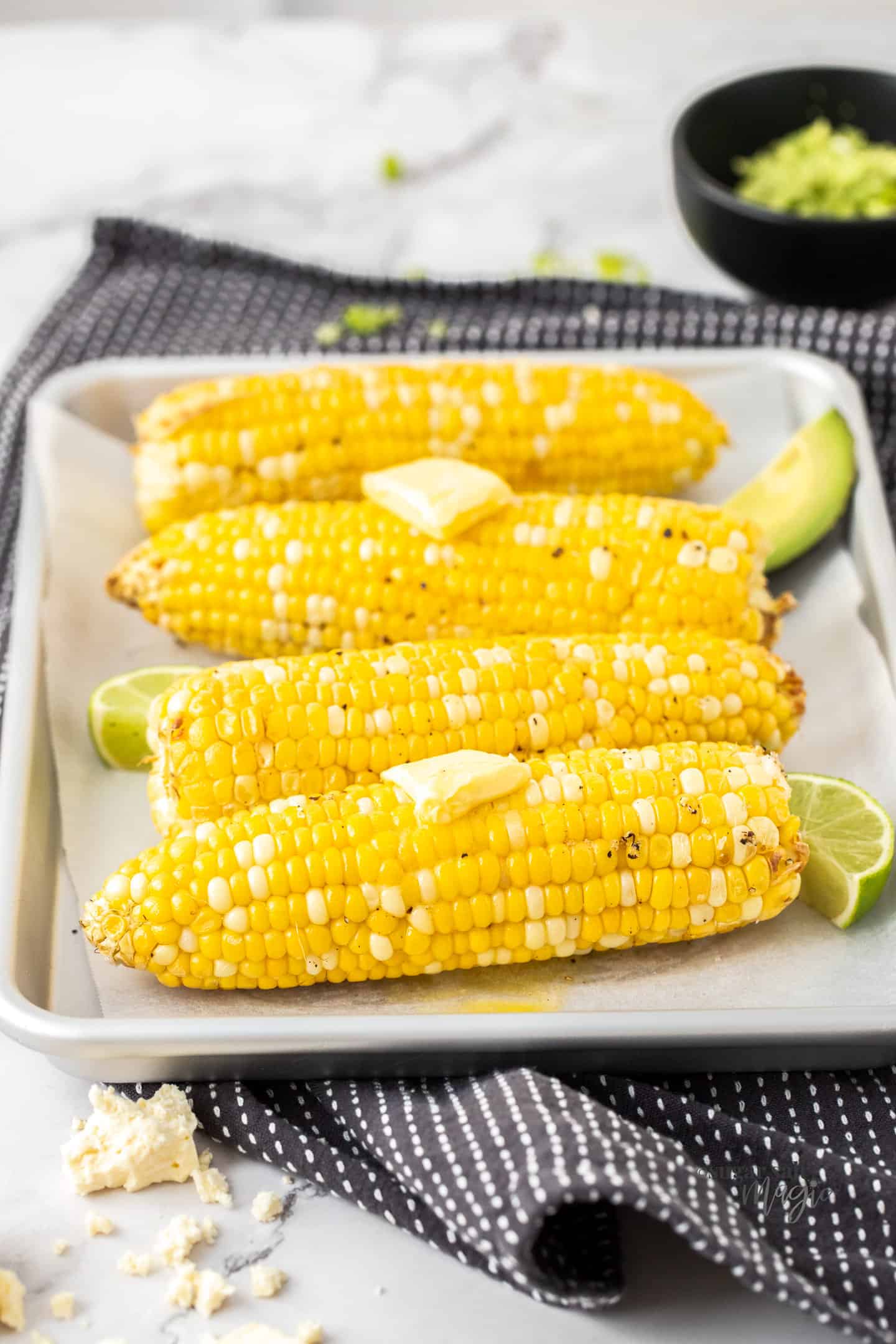 4 cobs of corn on a silver baking tray topped with butter.