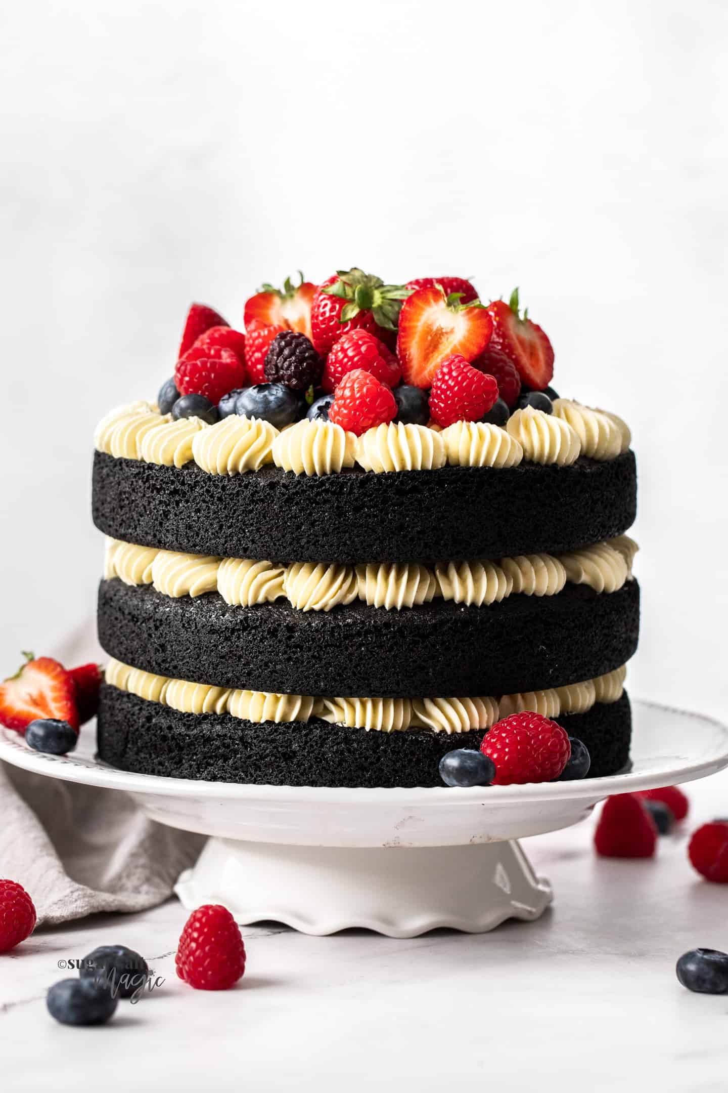 Front on view of a 3 tier black velvet cake topped with fresh berries.