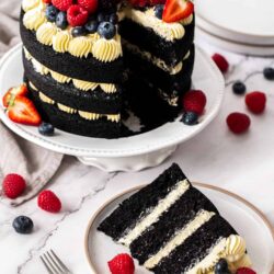 A 3 tier black velvet cake topped with berries, with a slice cut out.