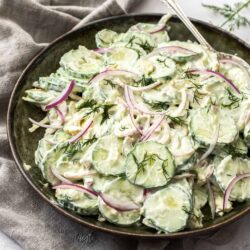 A dark green bowl filled with creamy cucumber salad.
