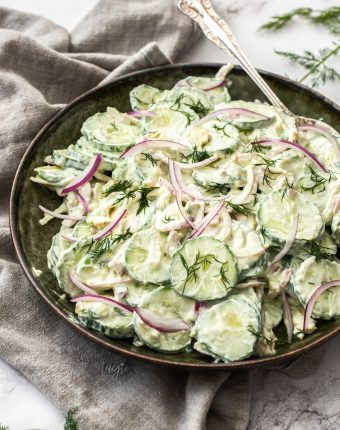 A dark green bowl filled with creamy cucumber salad.