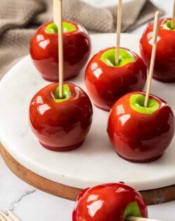 6 red toffee apples on a white marble platter.