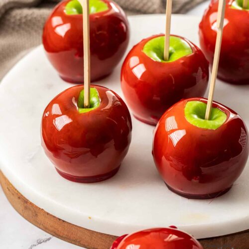6 red toffee apples on a white marble platter.