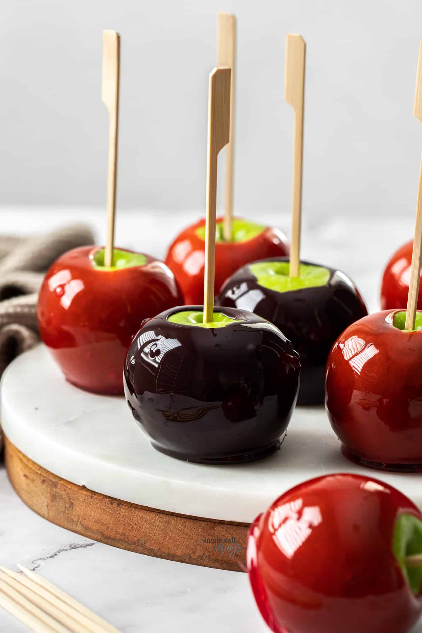 Red and black toffee apples on a white marble platter.