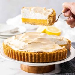 A slice of lemon meringue pie being held above the rest of the pie.