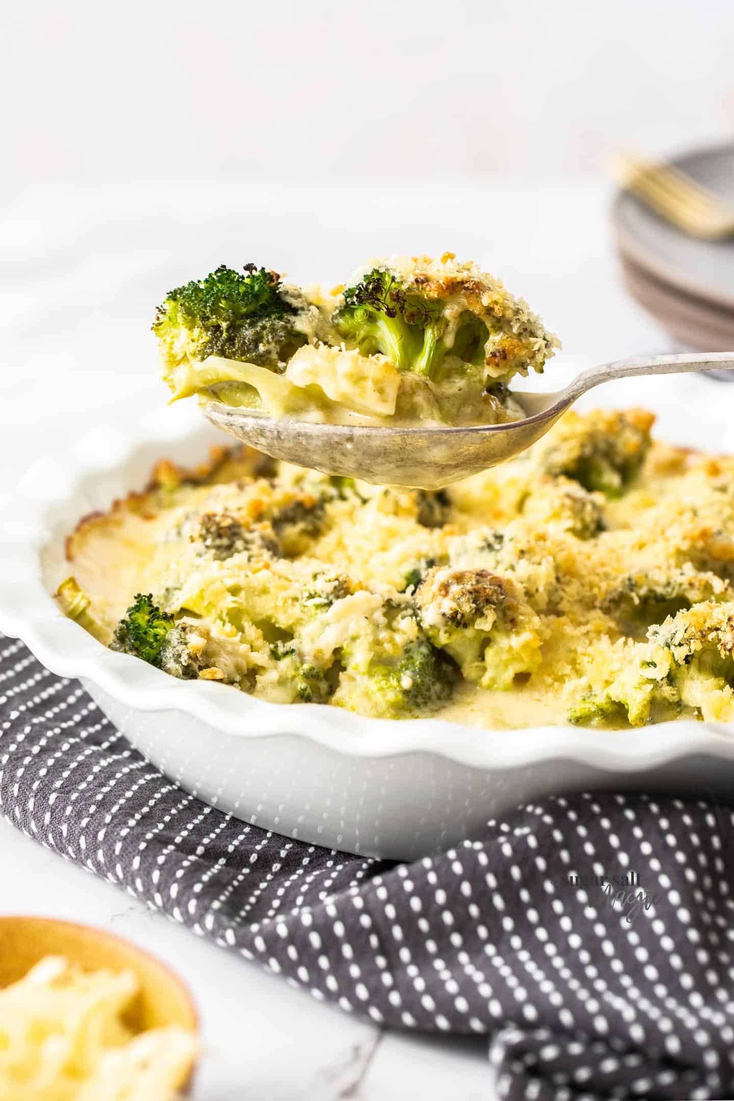 A spoon scooping broccoli cheese out of a baking dish.