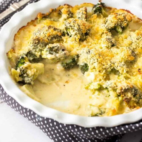 A pie dish filled with broccol cheese with a big scoop taken out.