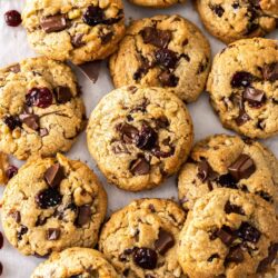 A big batch of walnut cranberry cookies on a sheet of baking paper.