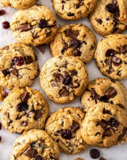 A big batch of walnut cranberry cookies on a sheet of baking paper.