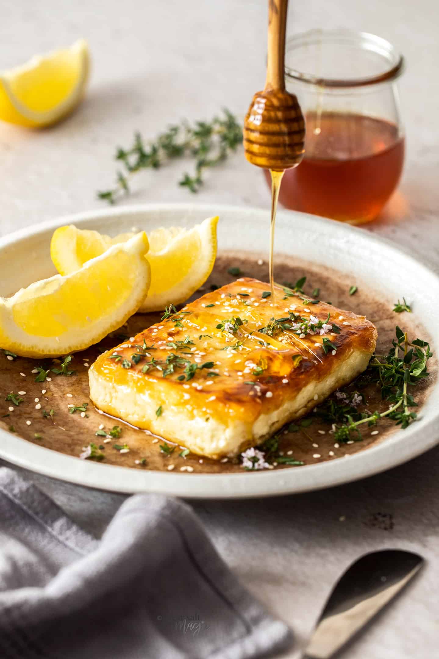 Honey being drizzled onto a square of pan-fried feta cheese.