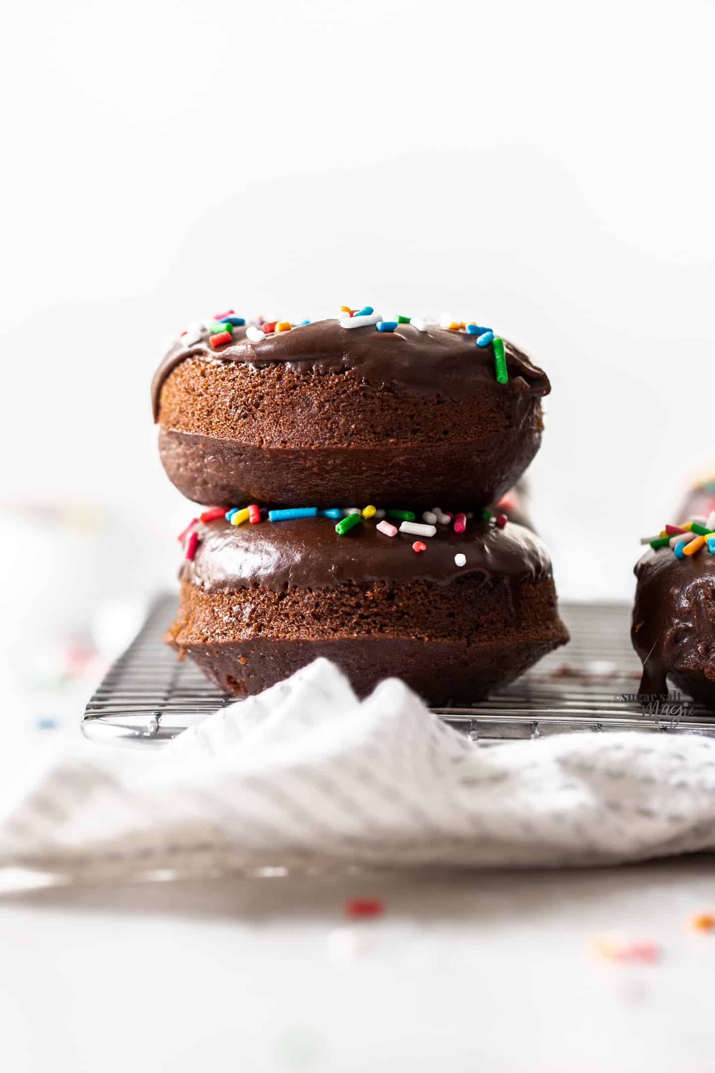 Two stacked chocolate cake donuts with sprinkles on top.
