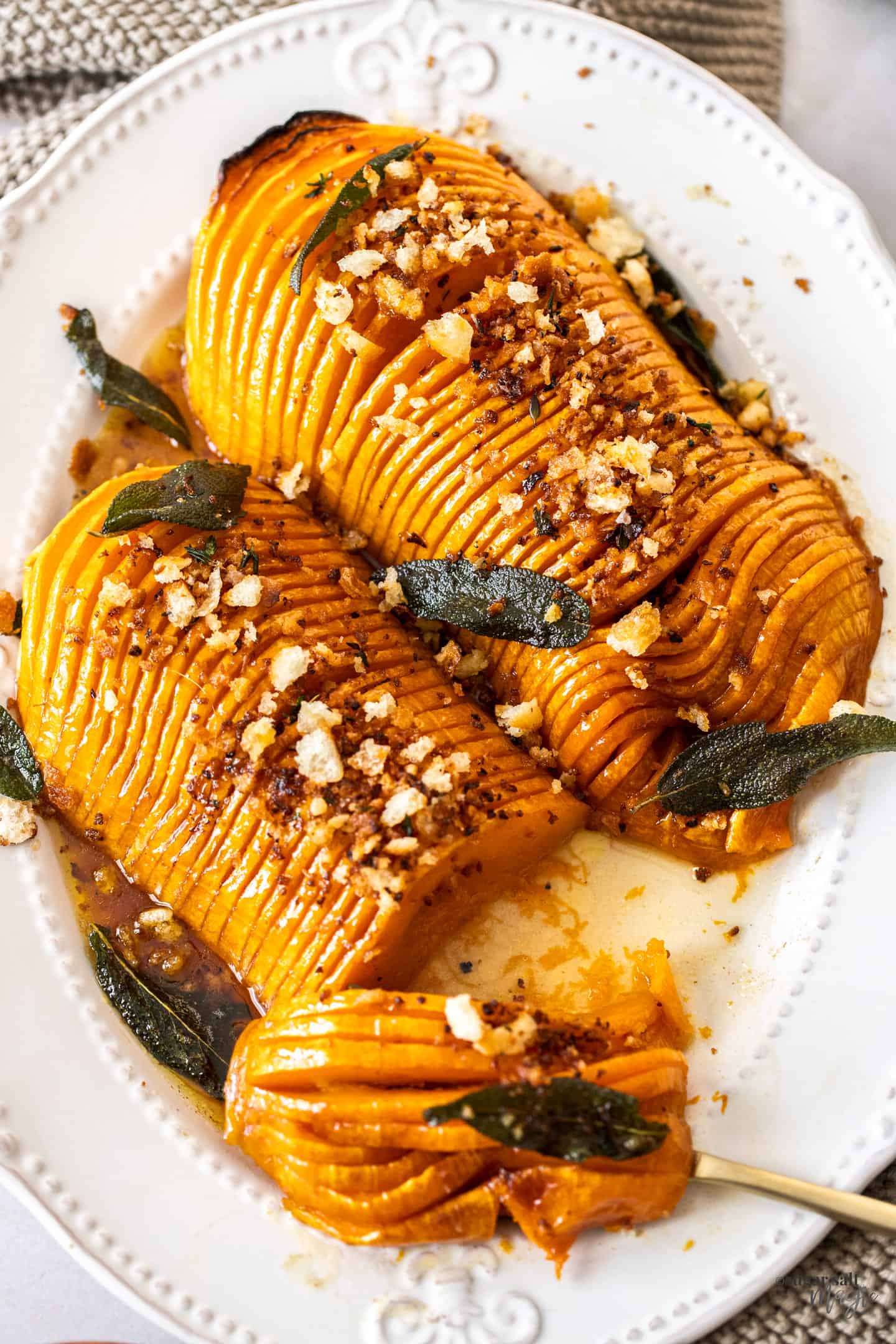 Two pieces of roasted hasselback butternut squahs on a white platter, with some cut away.