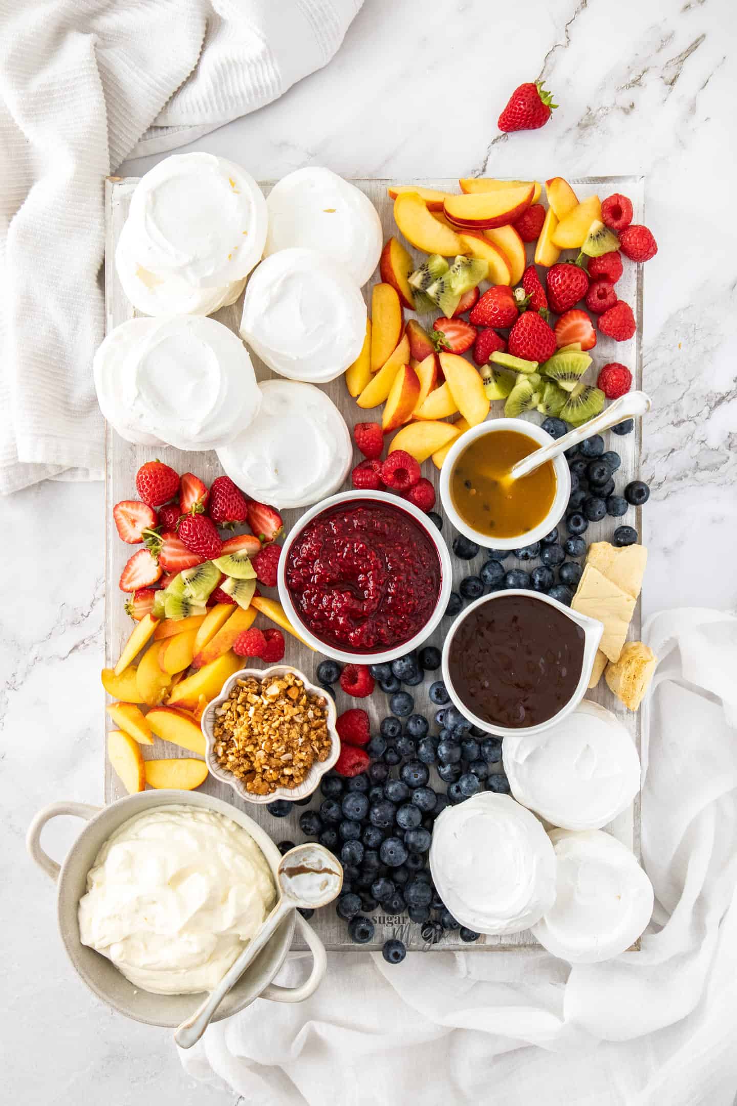 Top down view of a board filled with meringues, fruit and sauces.