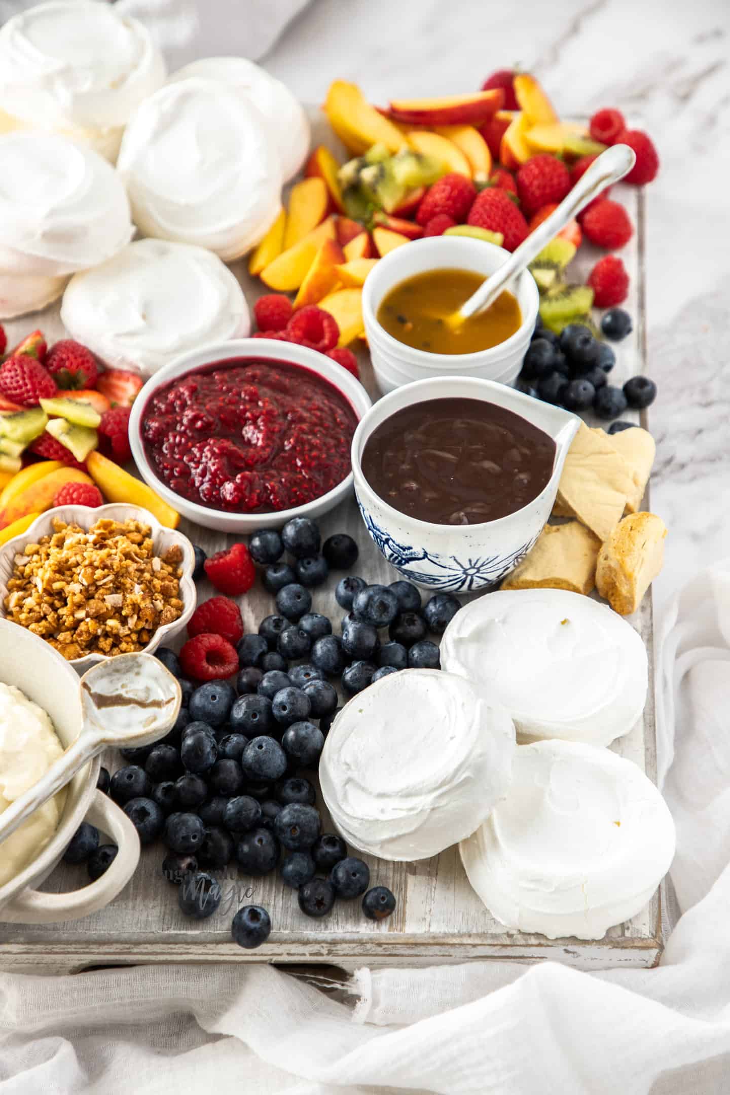 A board filled with meringue shells, sauces and fruit.