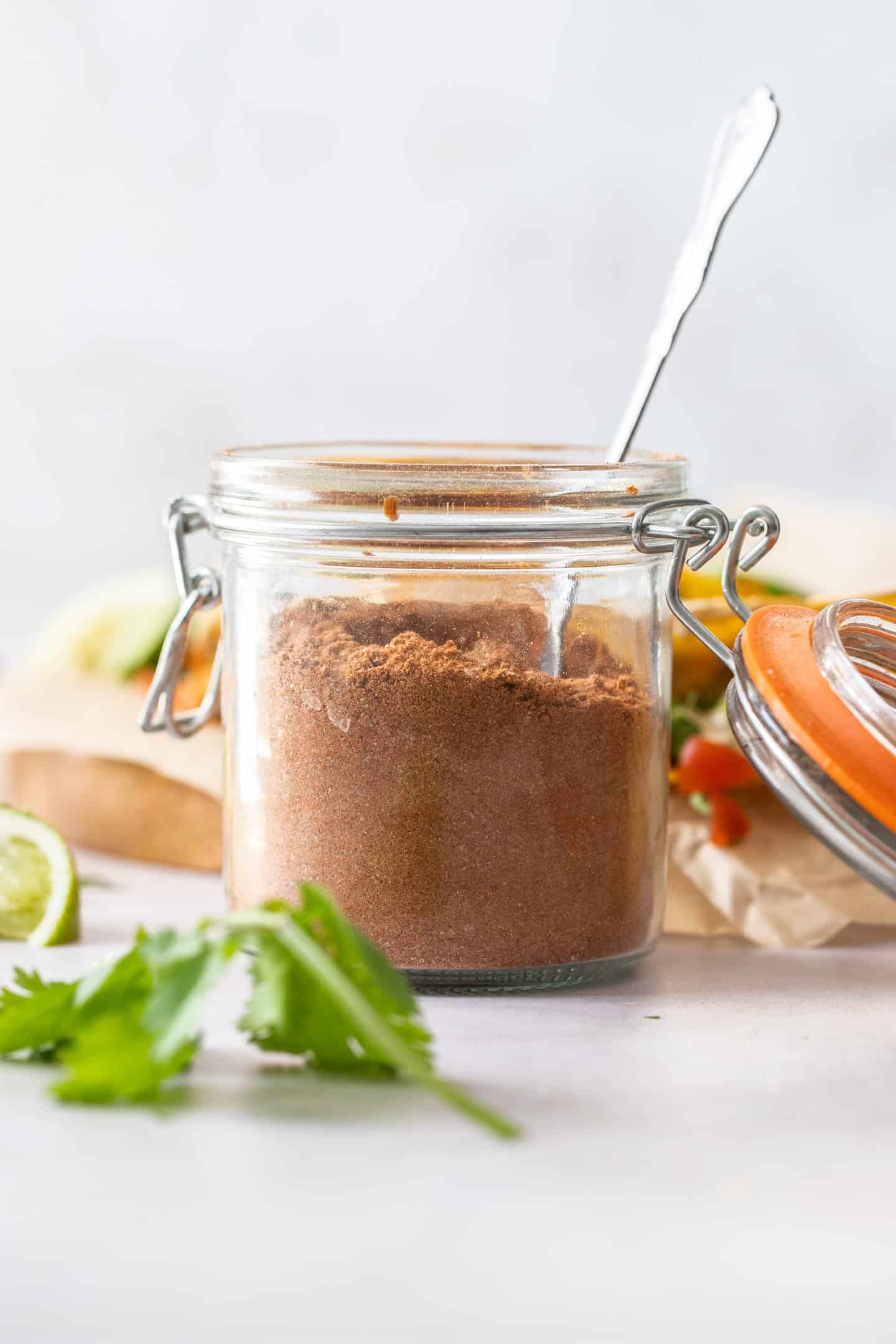 A small jar filled with taco seasoning with a spoon sticking out.