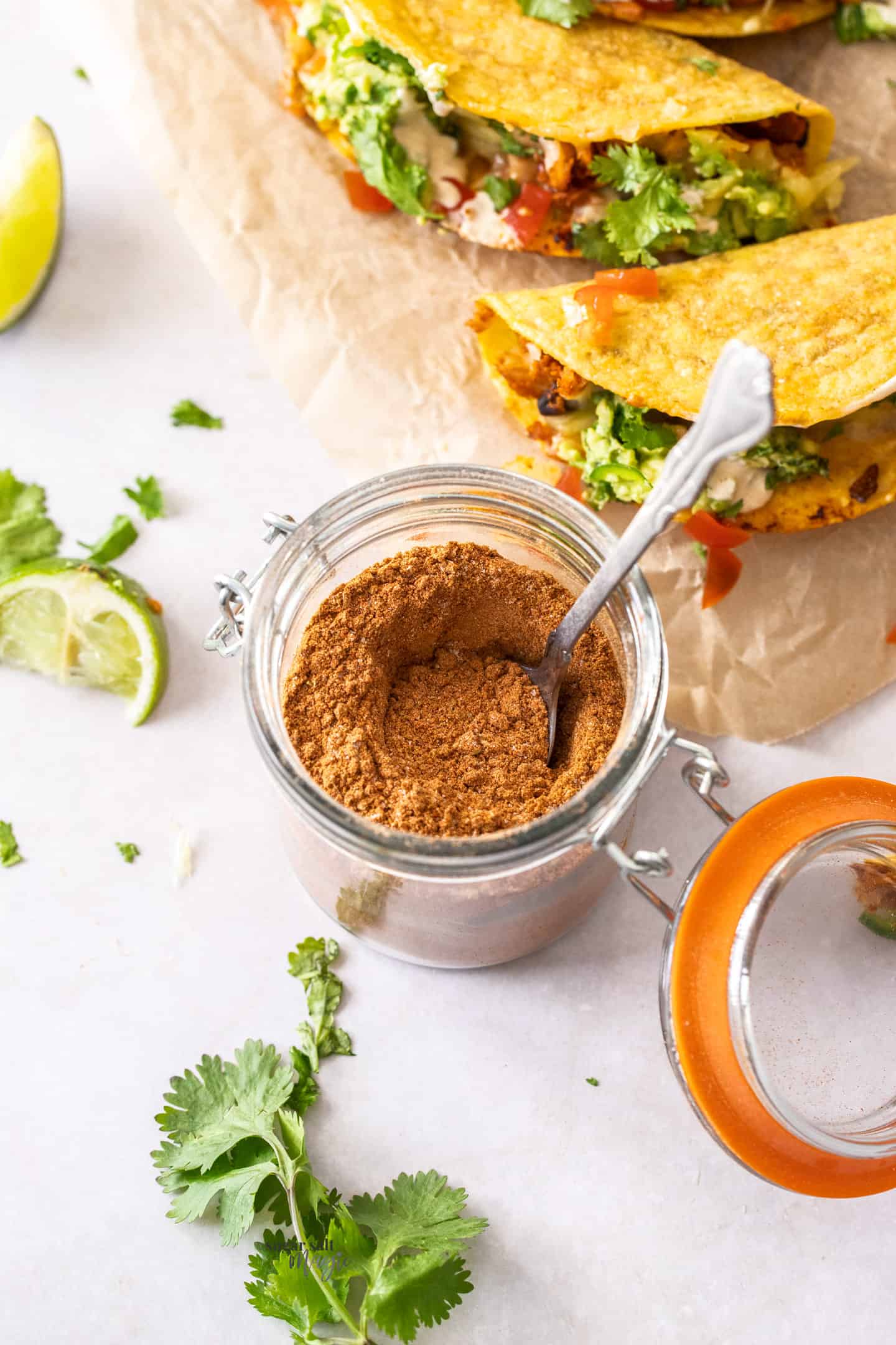 A small jar filled with taco seasoning. Tacos in the background.