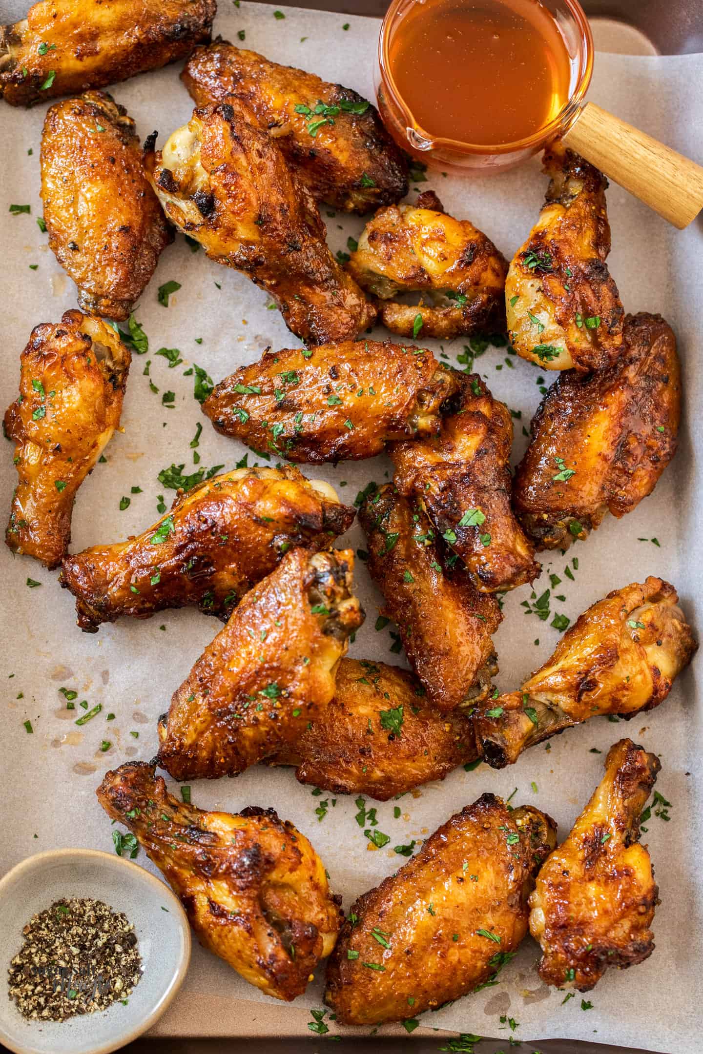 Golden baked chicken wings on a baking tray with a pot of honey.