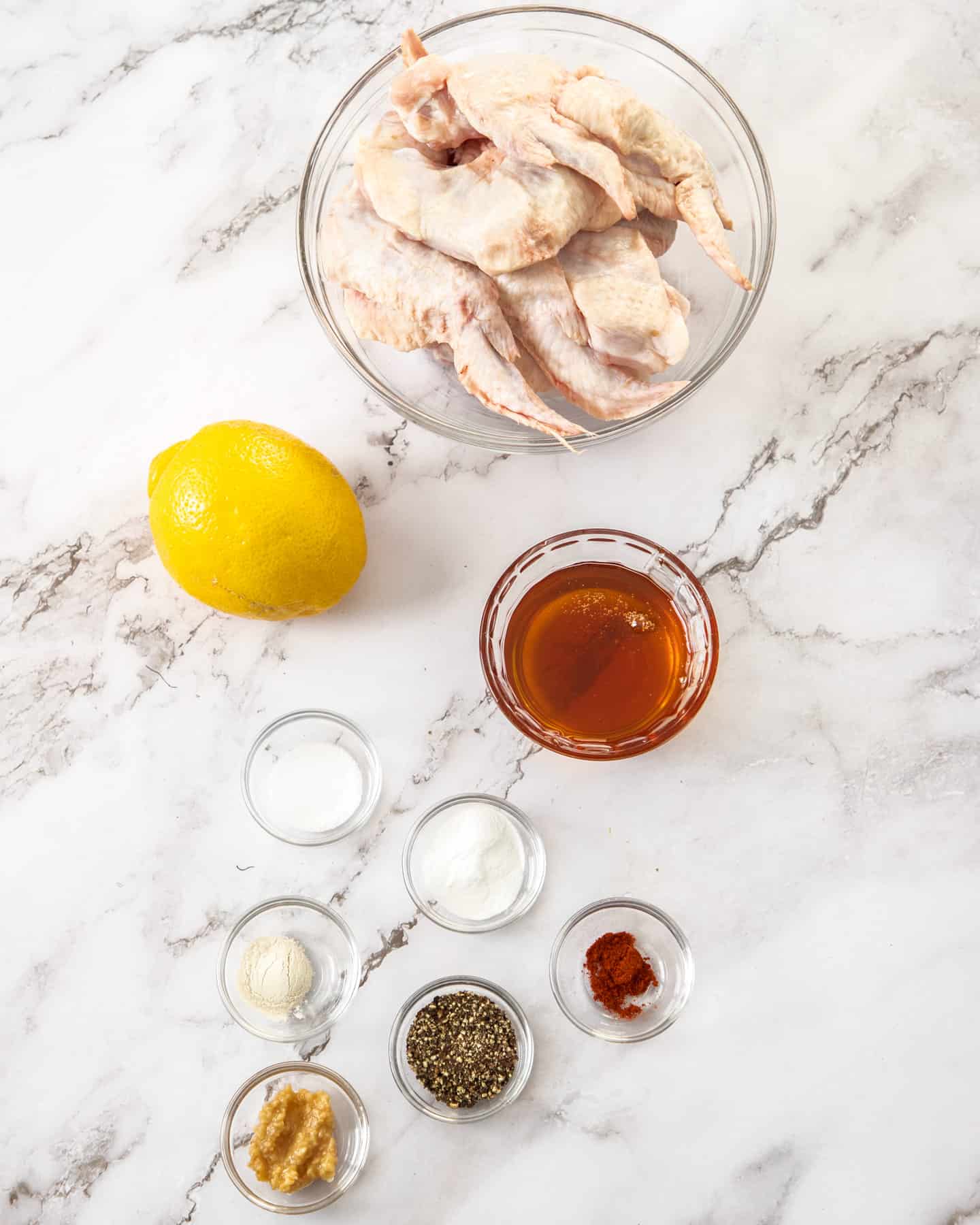 Ingredients for honey lemon pepper chicken wings on a marble benchtop.
