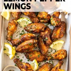 Baked golden chicken wings on a baking tray with lemon slices.