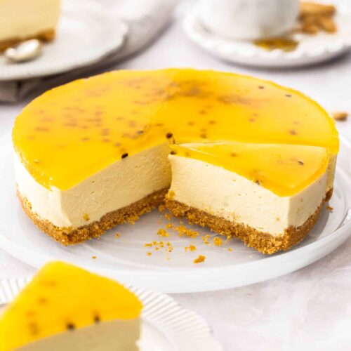 A passionfruit cheesecake with slices cut from it on a white platter.