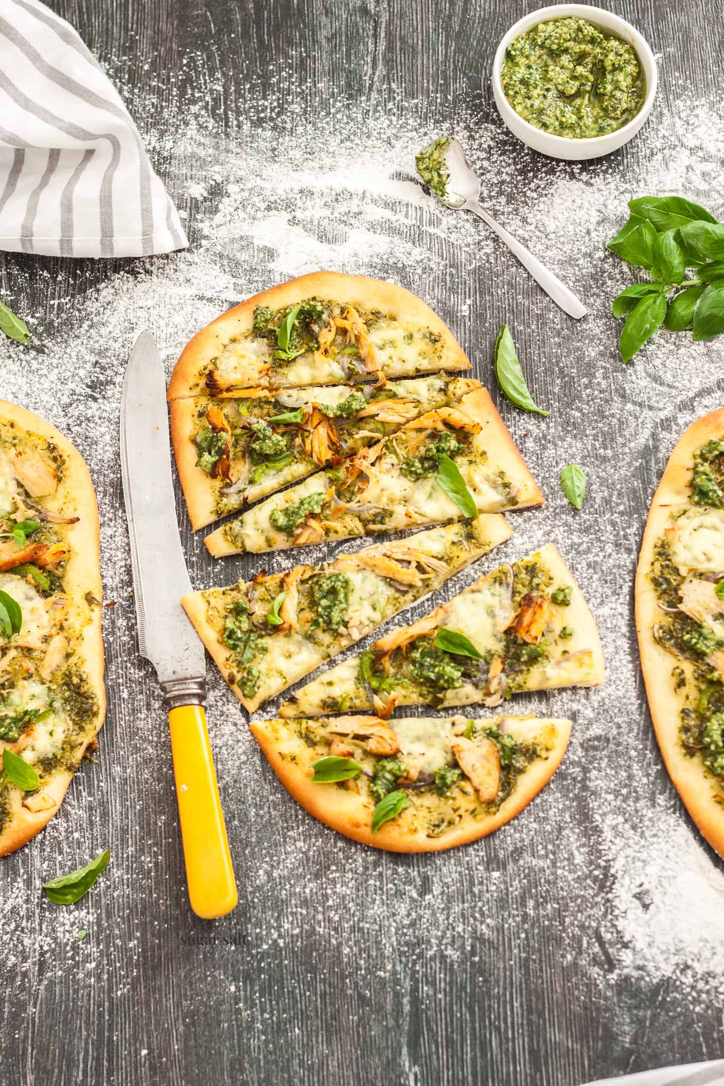 3 flatbreads topped with pesto and turkey, cut into slices, on a wood surface.