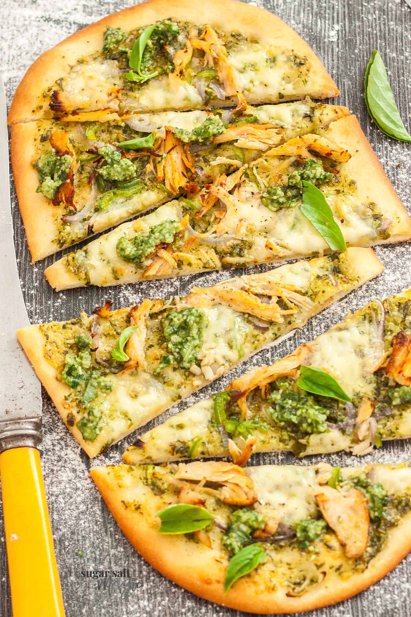 Flatbread topped with pesto and turkey, cut into slices, on a wood surface.
