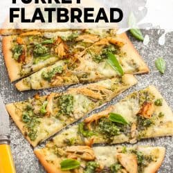 Flatbread topped with pesto and turkey on a dark wood surface.