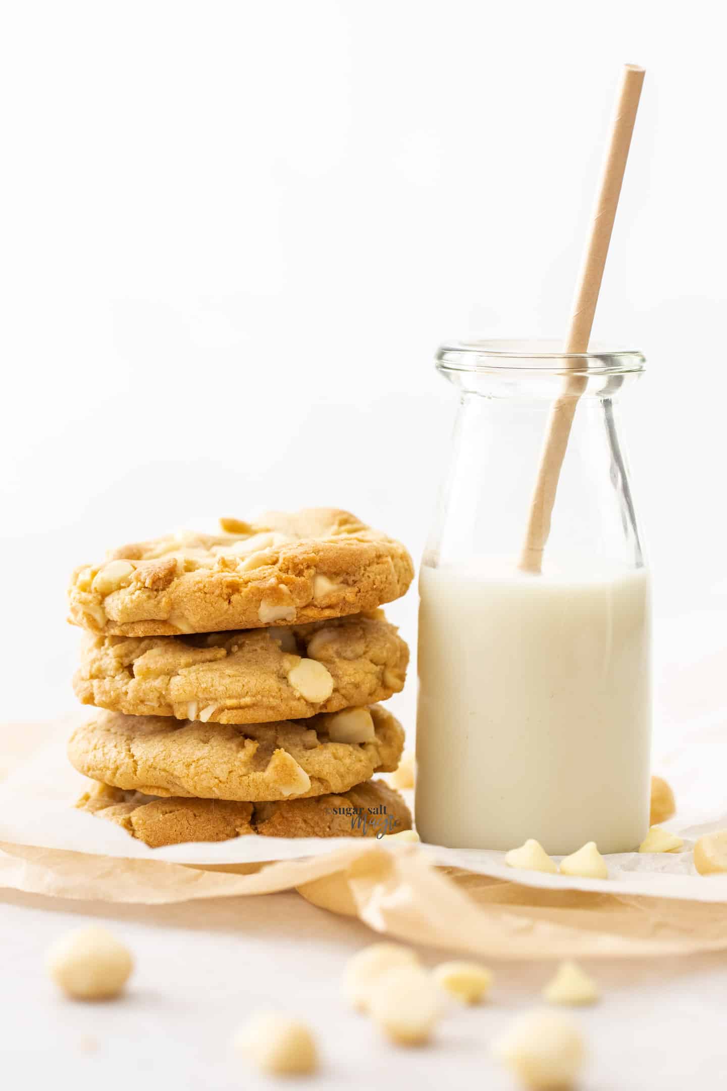 A stack of 4 cookies sitting up against a small bottle of milk.