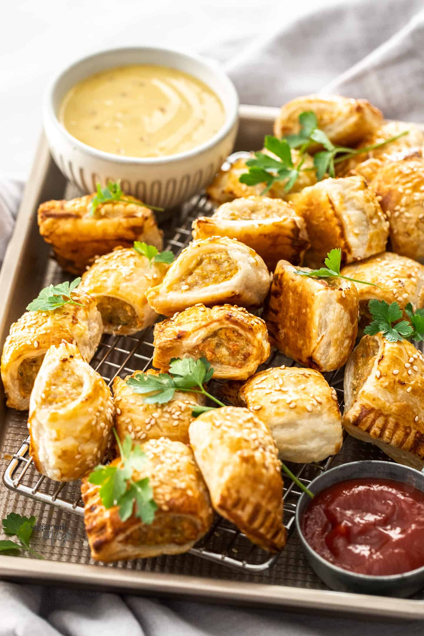 Chicken sausage rolls piled into a baking tray with a bowl of sauce at the back.