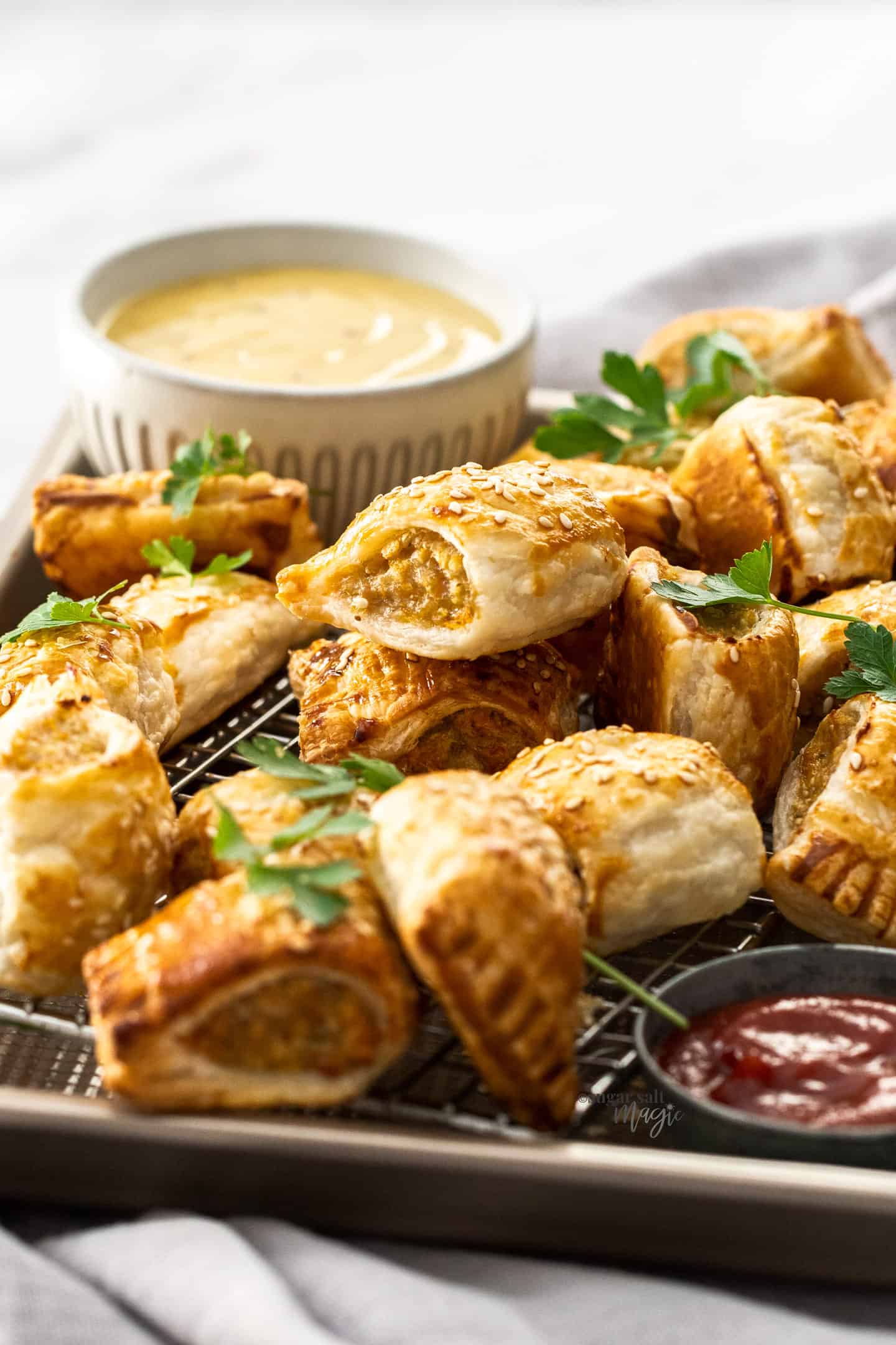 Chicken sausage rolls piled into a baking tray with a bowl of sauce in the background.