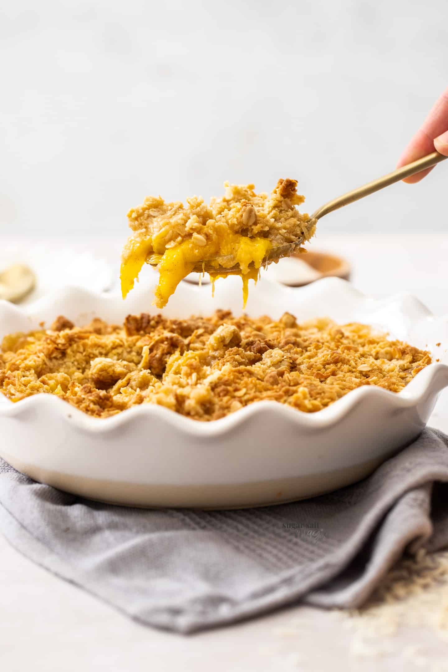 A gold spoon scooping mango crumble out of a pie dish.