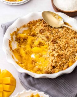A pie dish filled with mango crumble with some scooped out.