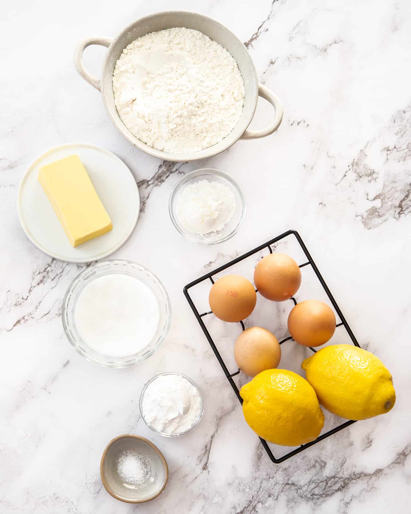 Ingredients for lemon tartlets on a marble surface.
