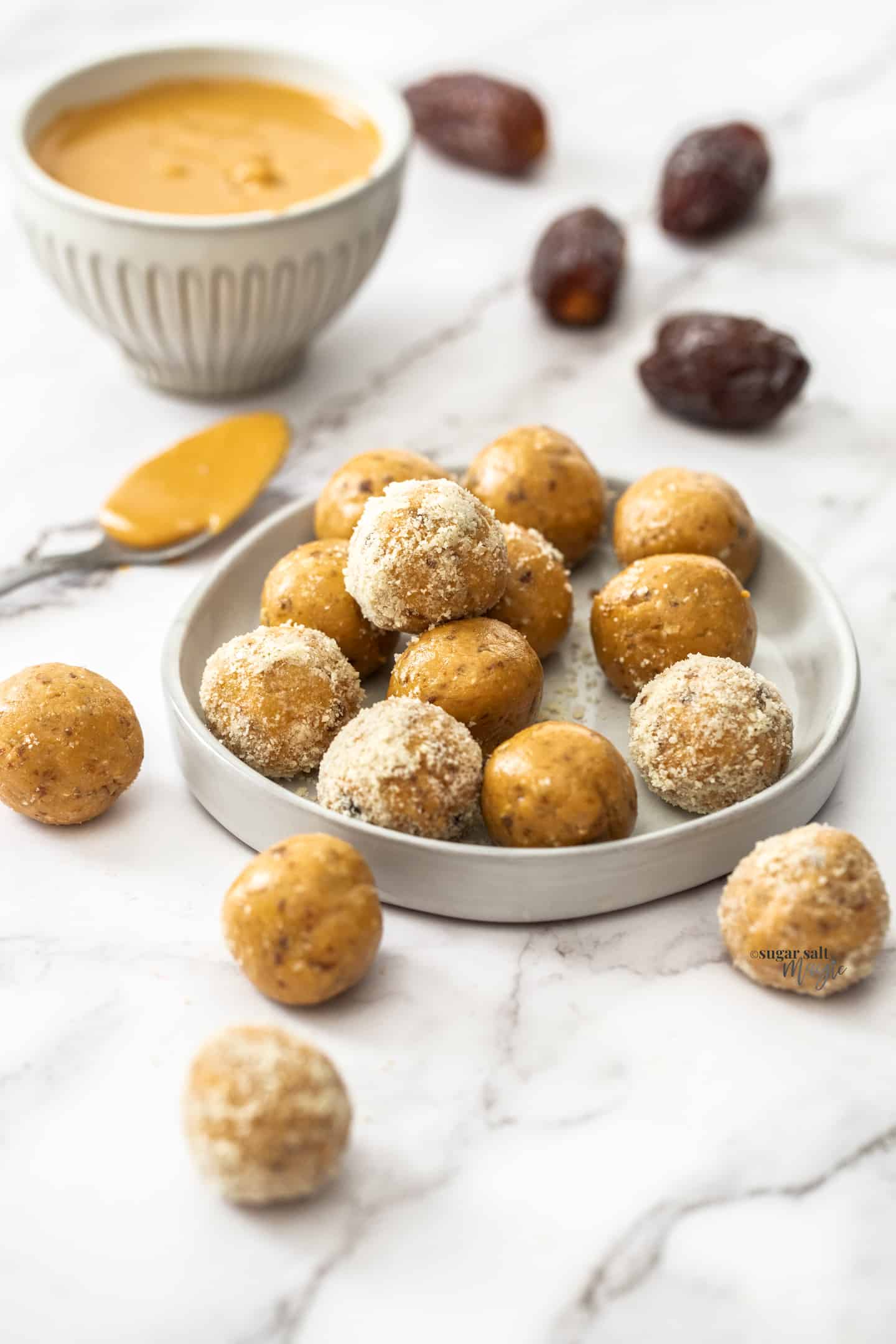 A batch of peanut butter bliss balls on a small dish with dates in the background.