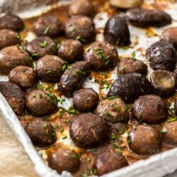 Roasted mushrooms on a foil lined baking tray scattered with chives.