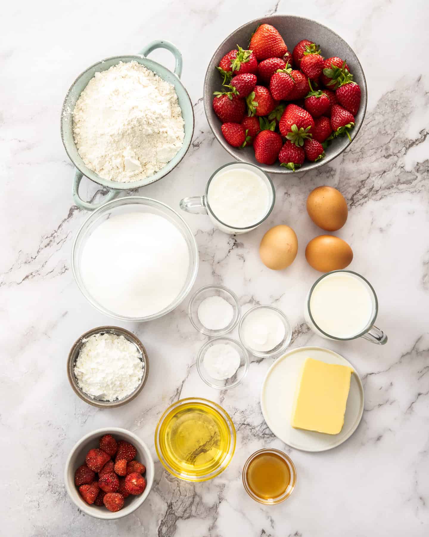 Ingredients for strawberry sheetcake on a marble benchtop.