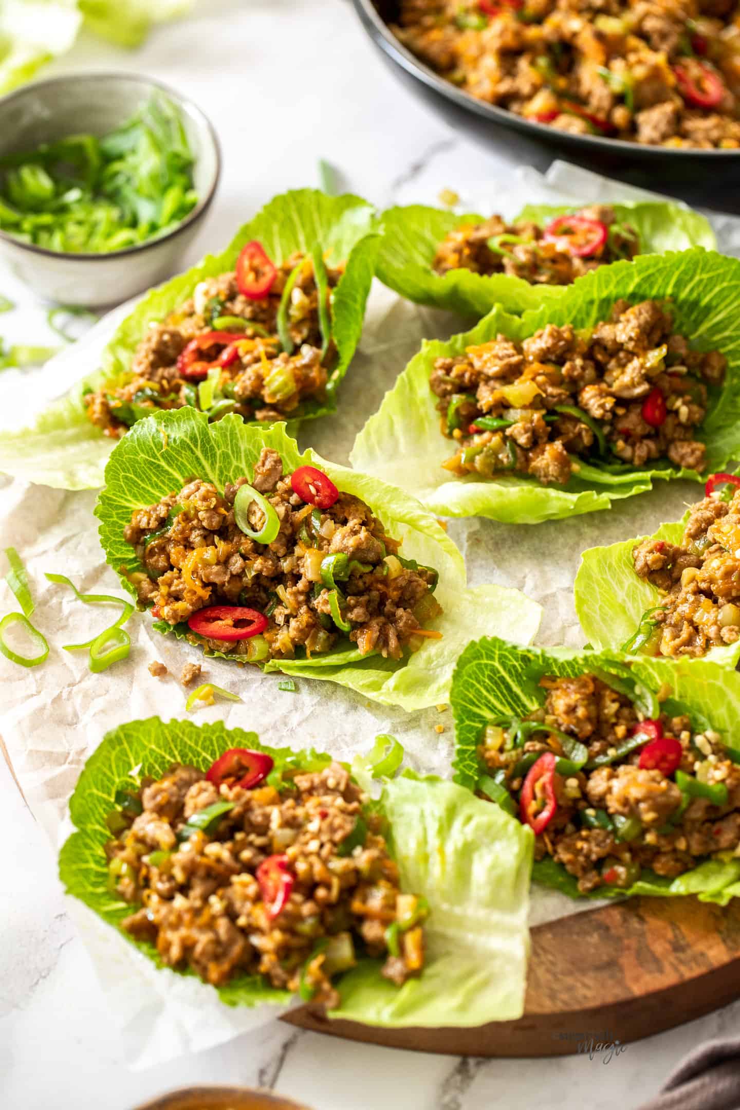 A wooden platter topped with lettuce leaves filled with turkey san choy bow filling.
